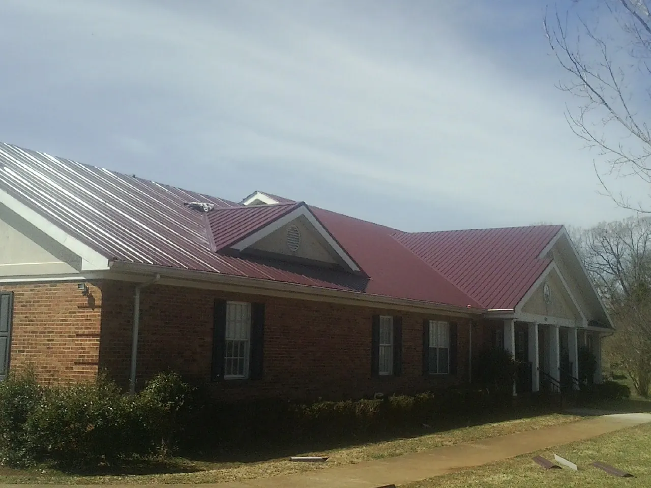 Red metal roof with gabled entries on a long brick building, from a Hail Damage Roof Repair job in Cornwall