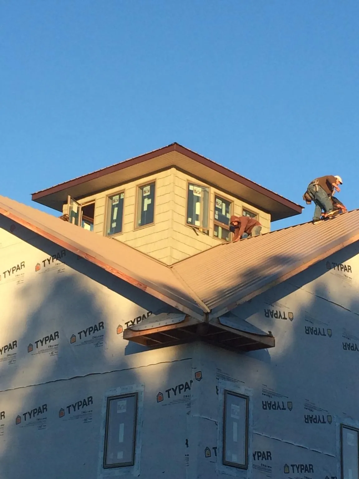 Roofers working around a rooftop cupola on a new metal roof at sunset — Roof Waterproofing in Cornwall by Roofing Brothers
